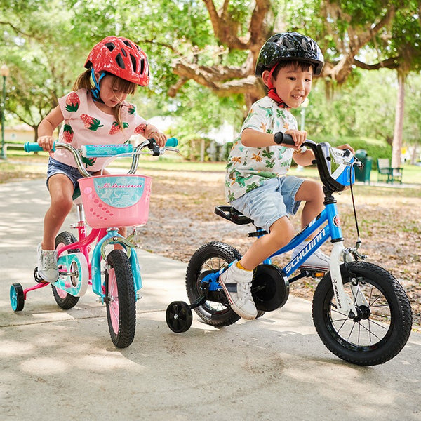 Two kids learning how to ride their bikes with training wheels