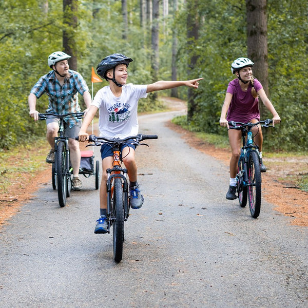 A family of three riding bikes on a path together and wearing helmets.