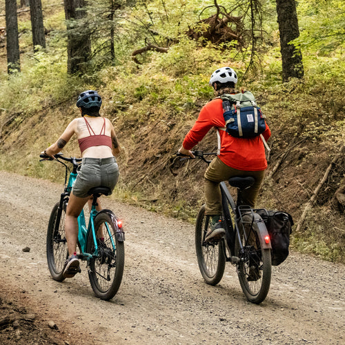 Two people riding Coston E-bikes through a wooded path