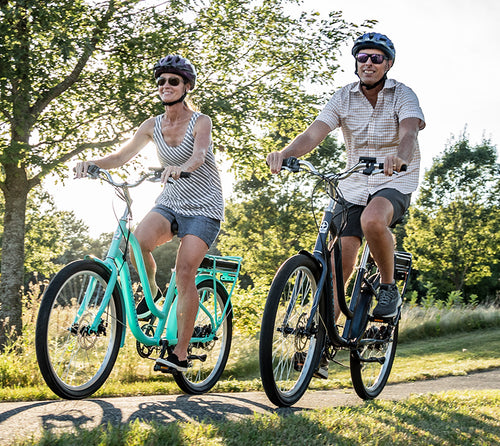 A couple riding Schwinn Mendocino E-bikes at sunset through a park.